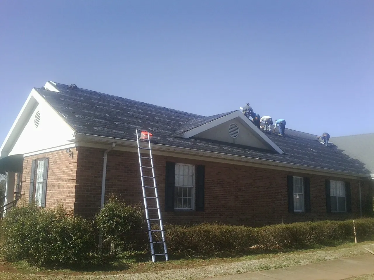 Crew tearing shingles off a brick ranch roof with a ladder set — Emergency Roof Repair work by our crew in Kewanna