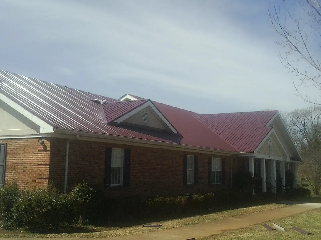 Red metal roof with gabled entries on a long brick building, from a Hail Damage Roof Repair job in Kewanna
