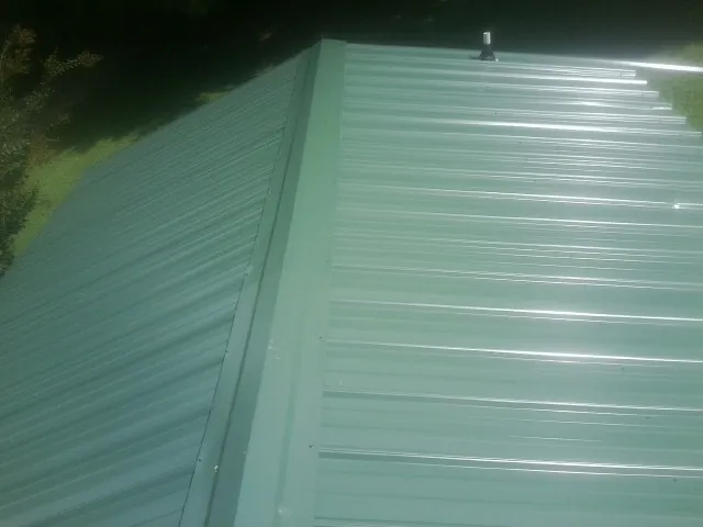 New green metal panels meeting at the ridge of a roof — Flat Roof Repair work by our crew in Kewanna