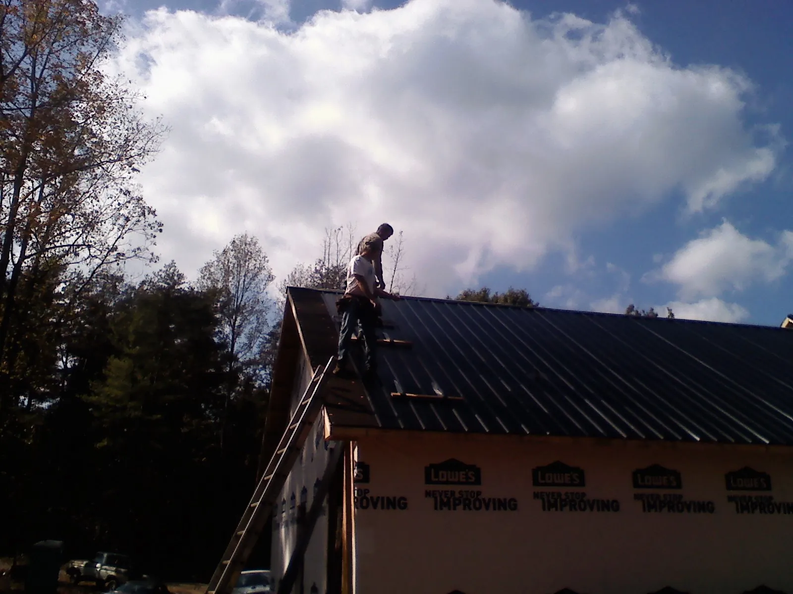 Roofer fastening dark metal panels high against a cloudy sky, from a Roof Inspection job in Kewanna