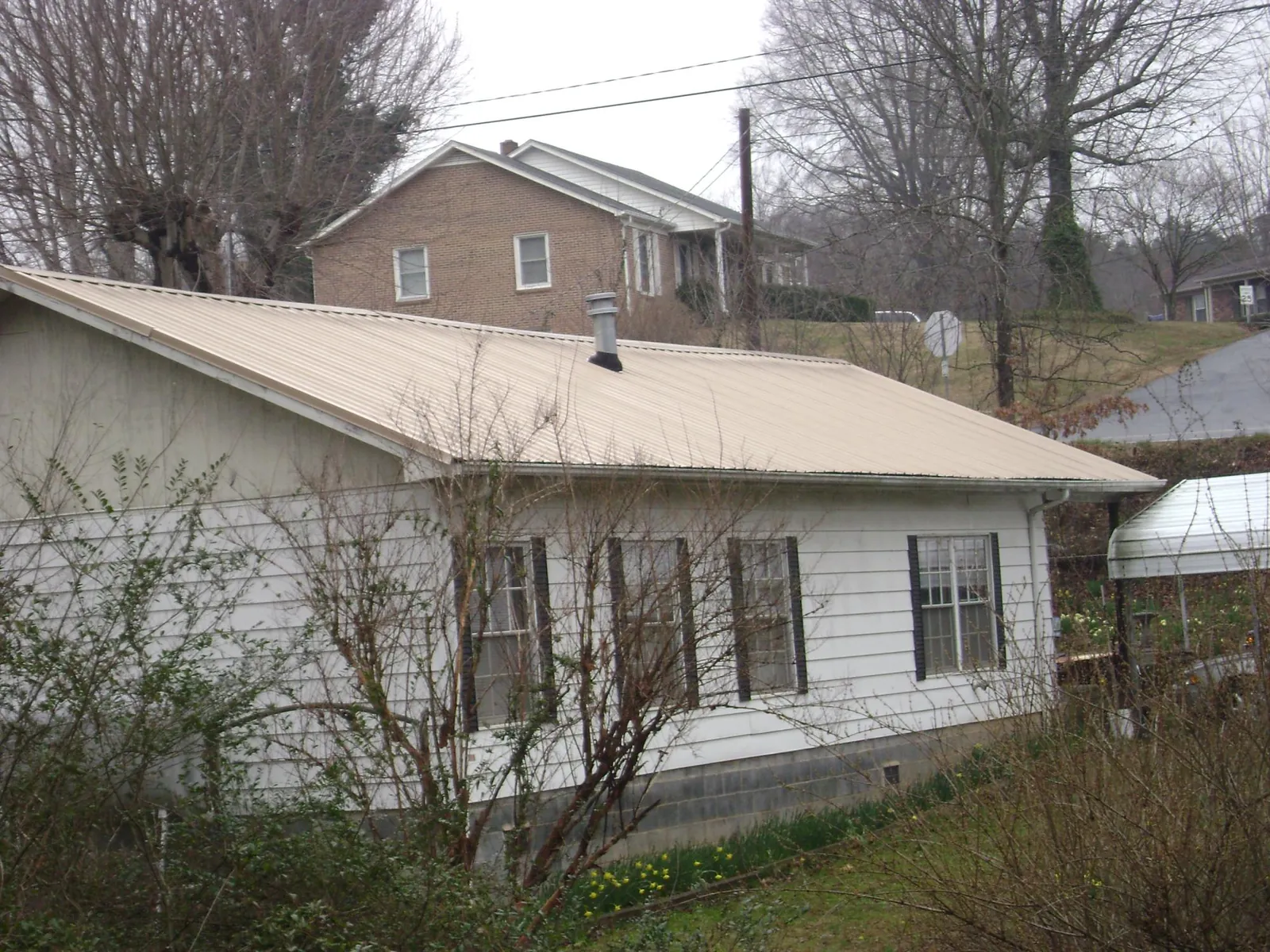 Tan metal roof on a white sided house set into a hillside — Commercial Roofing by Roofing Brothers in Kewanna