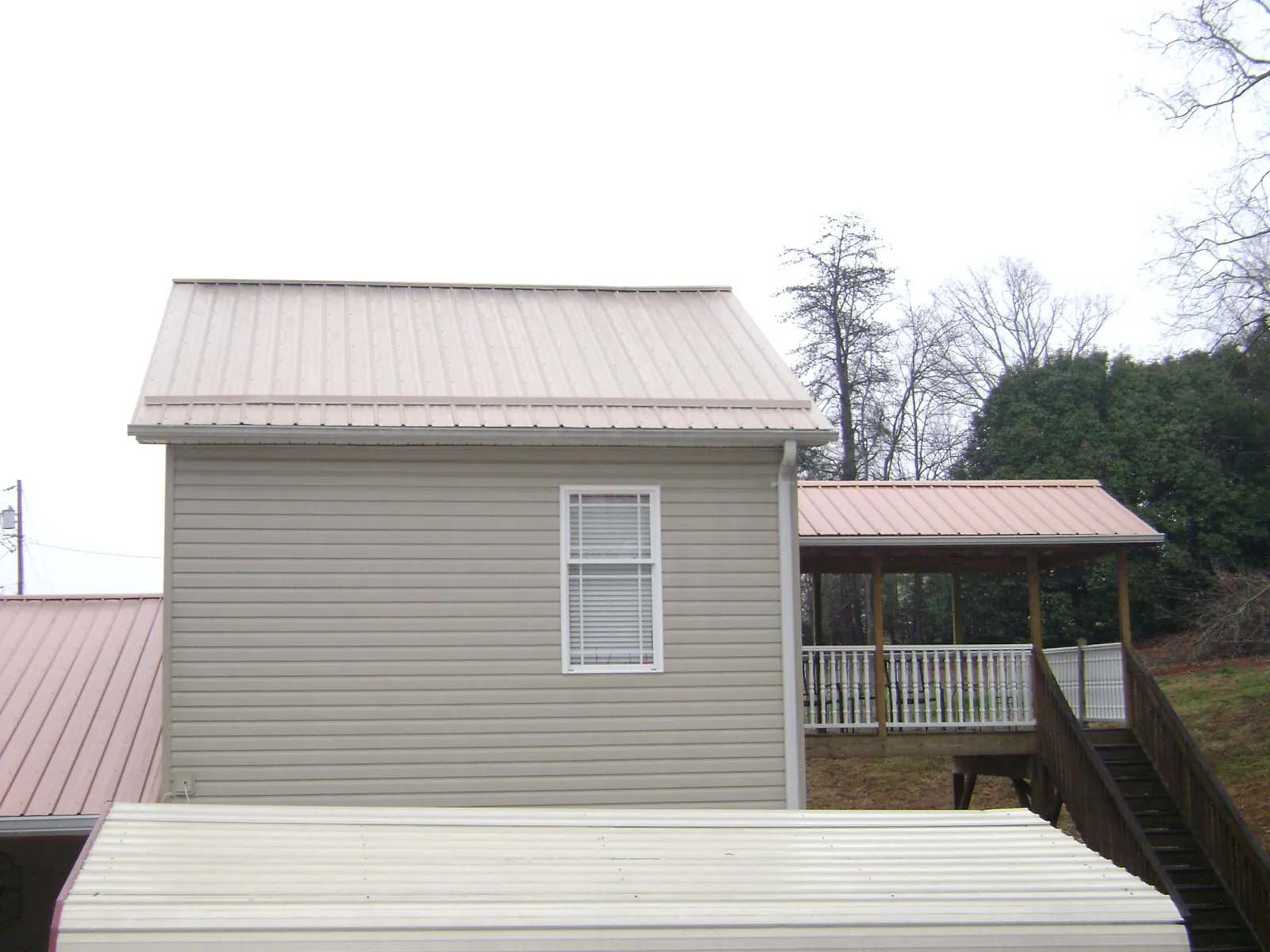 Tan metal roofs on a two story addition and attached porch, from a Roof Replacement job in Kewanna